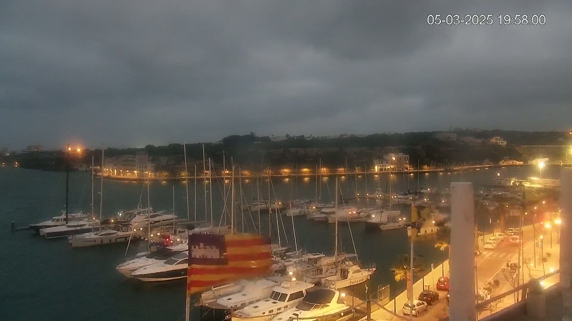 Many boats are moored in a harbor at dusk under a cloudy sky.