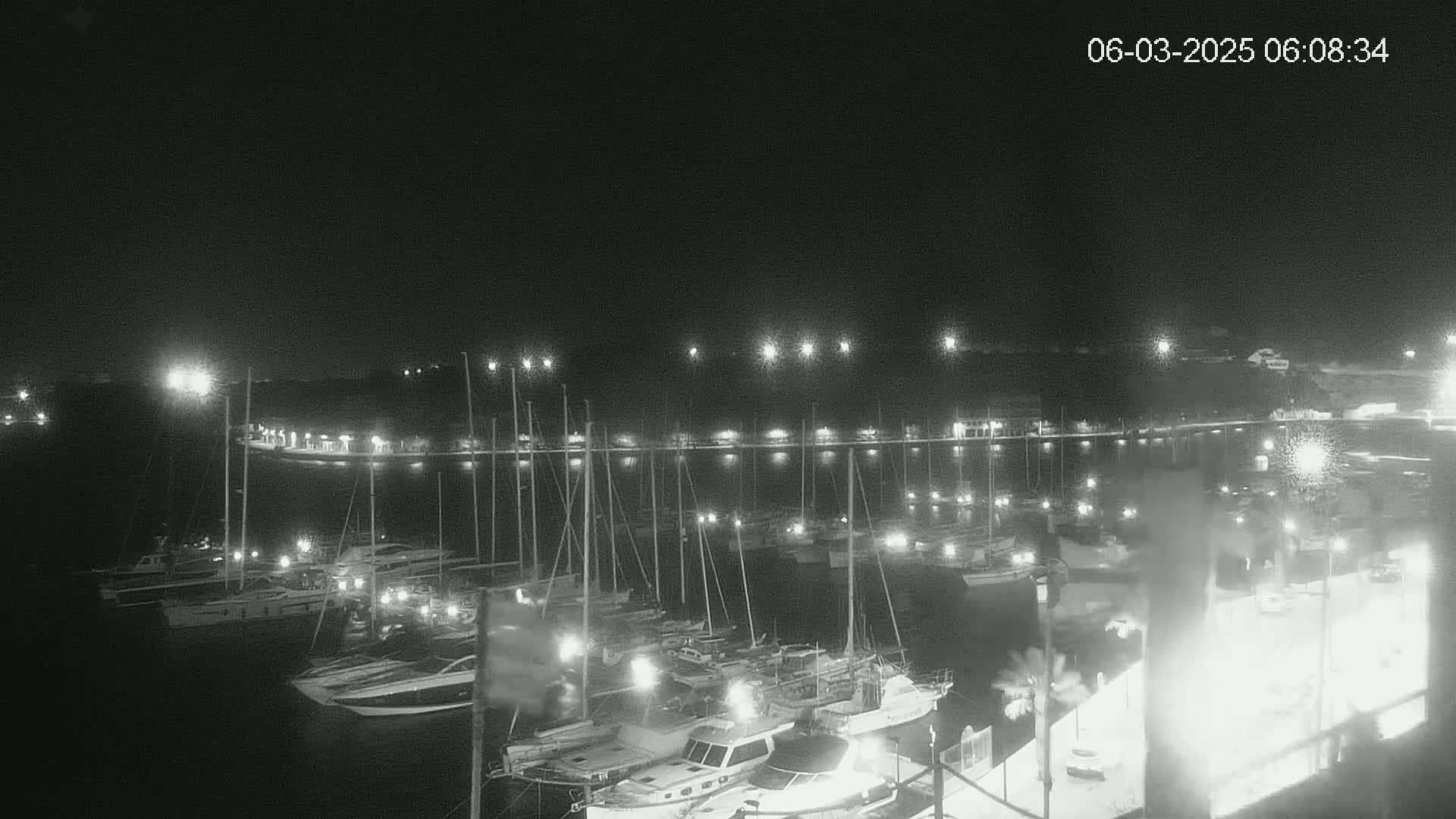 A nighttime view of a marina filled with numerous boats and yachts illuminated by lights under a clear, dark sky.