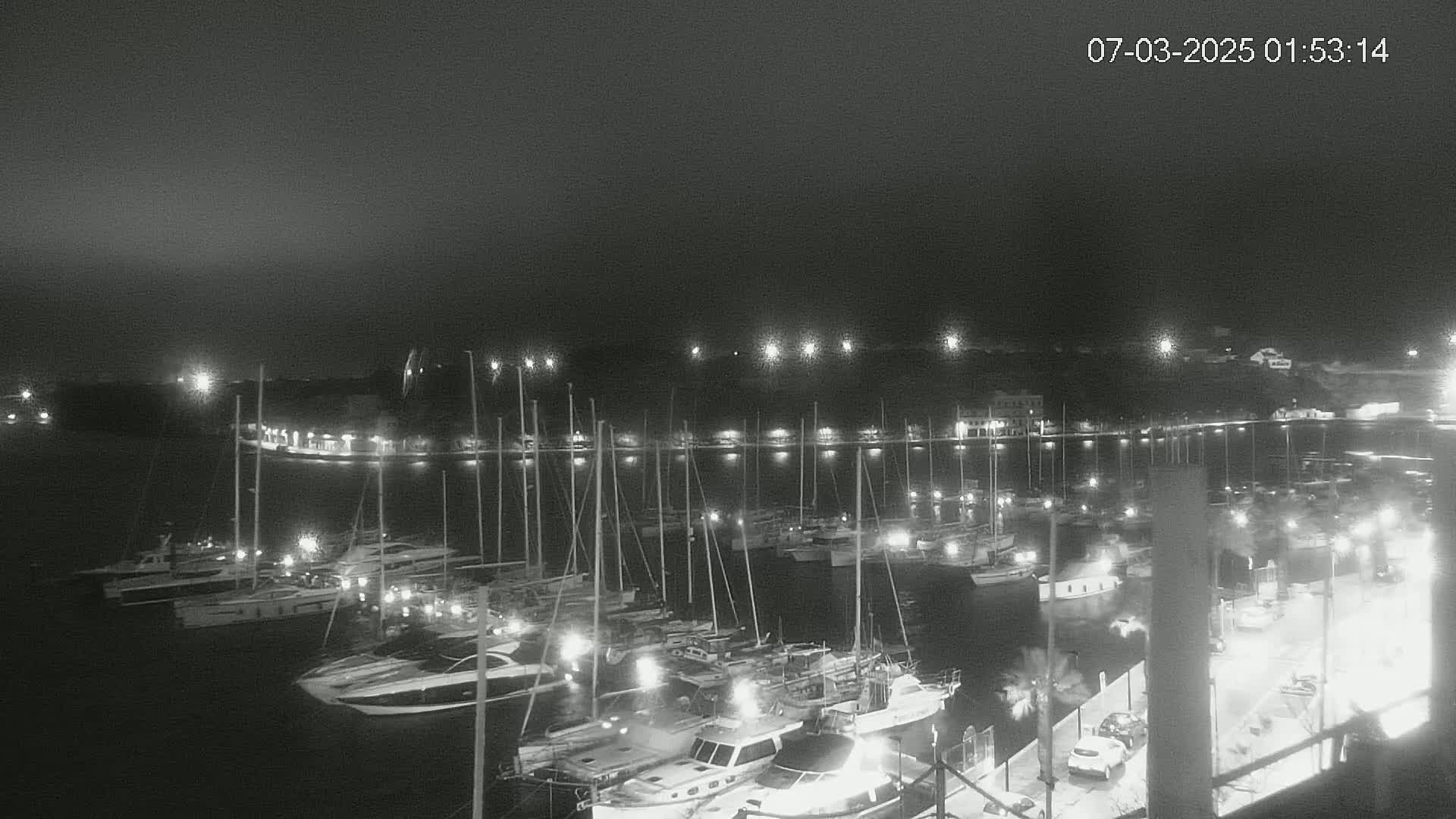A nighttime, low-light view of a marina filled with numerous boats and yachts, illuminated by lights along the shoreline.
