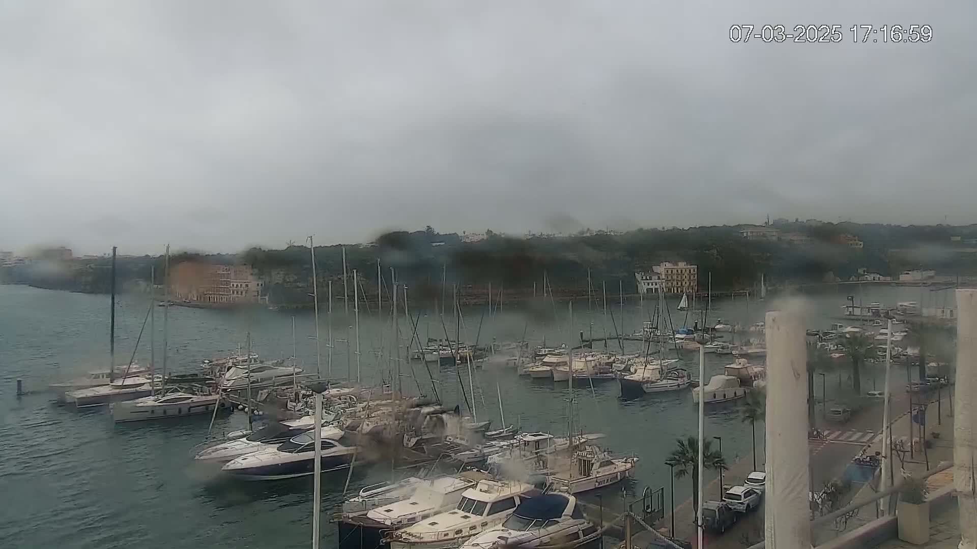 A marina filled with numerous boats is seen on an overcast, rainy day.