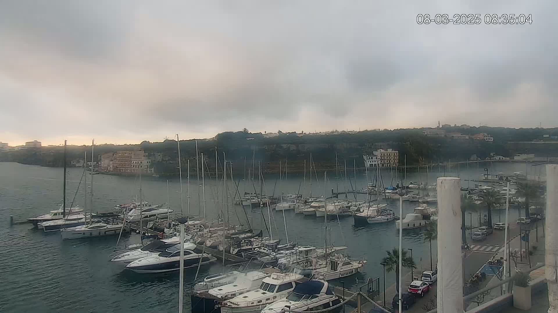 A marina filled with numerous boats and yachts is seen under an overcast sky.