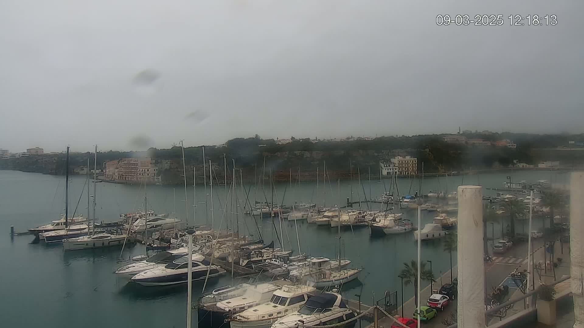 A harbor filled with numerous sailboats and motorboats is viewed on an overcast day.