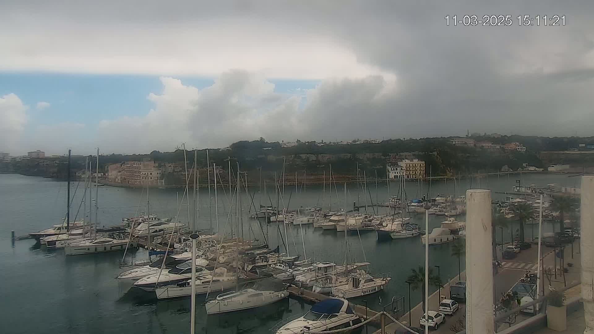 A harbor filled with numerous sailboats and motorboats under a mostly cloudy sky.