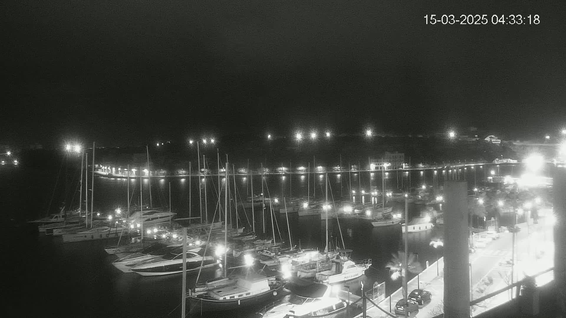 A nighttime harbor scene shows numerous boats moored at docks under a dark sky.