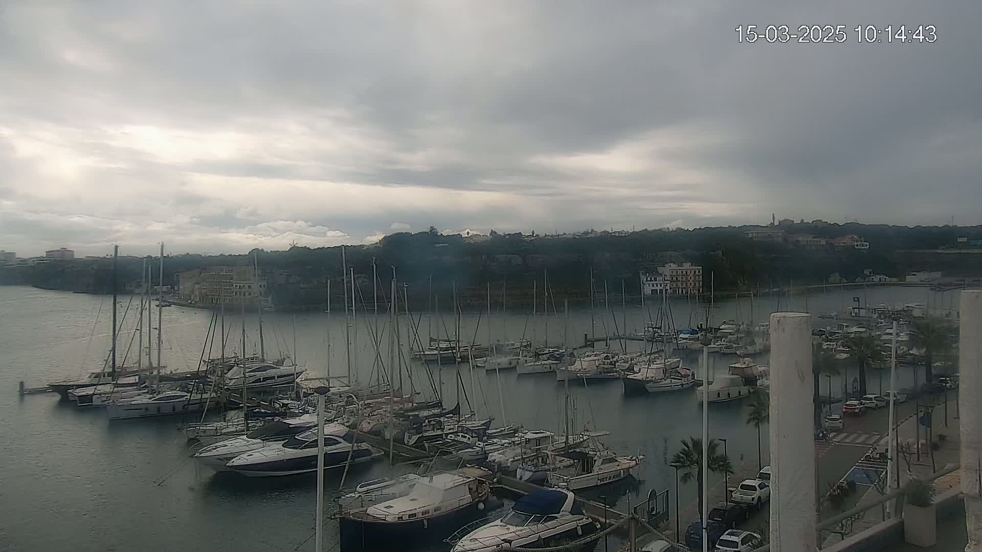 Many sailboats and motorboats are docked in a harbor under a cloudy sky.