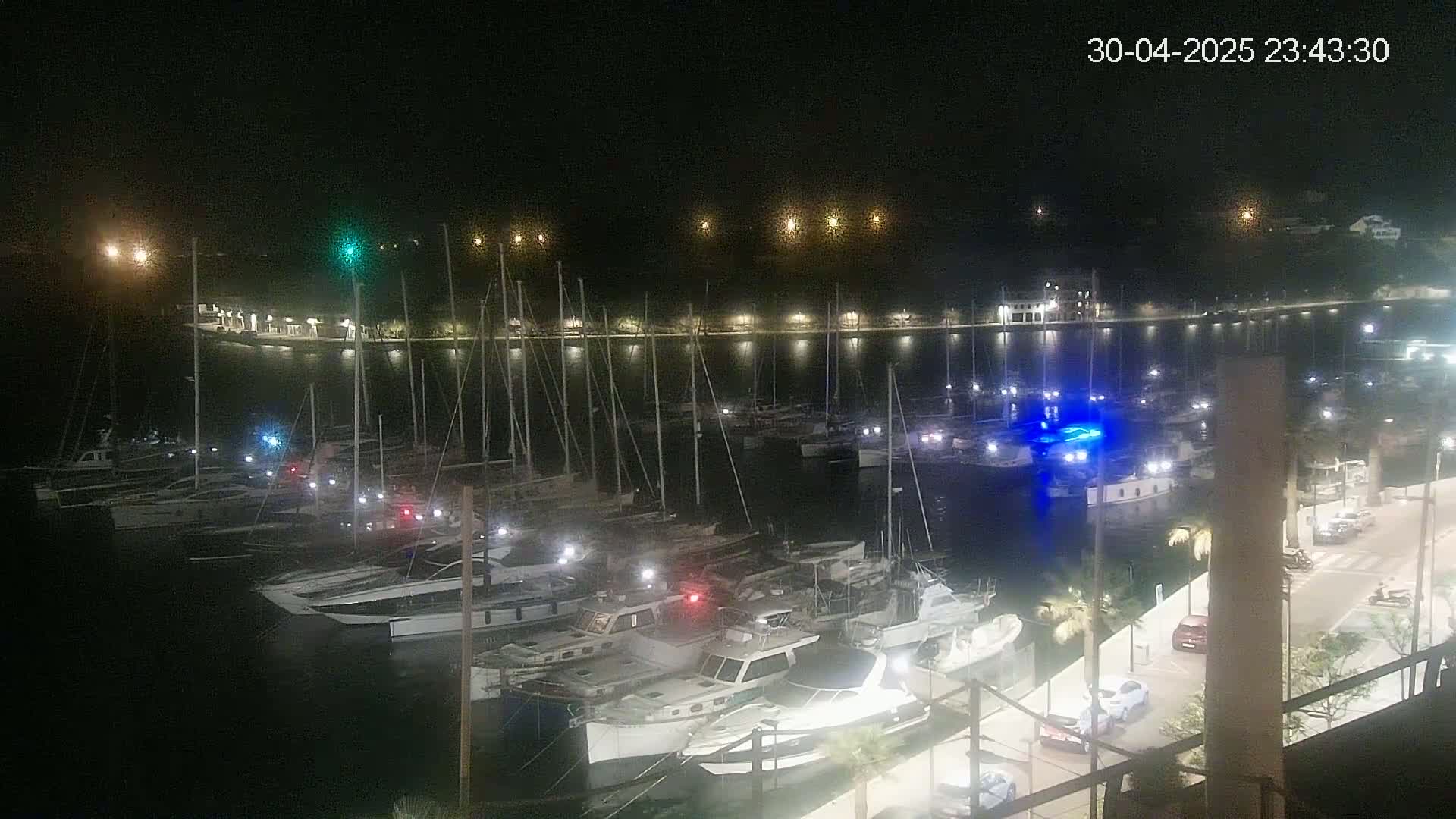 A nighttime view of a marina filled with boats docked along a waterfront, illuminated by lights from the shore and boats.