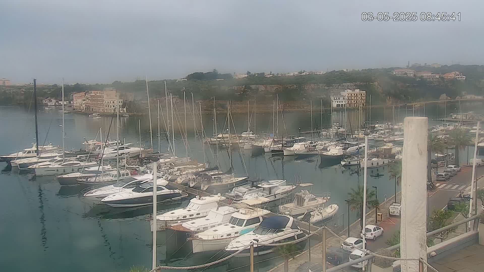 A marina filled with numerous sailboats and motorboats is viewed on an overcast day.