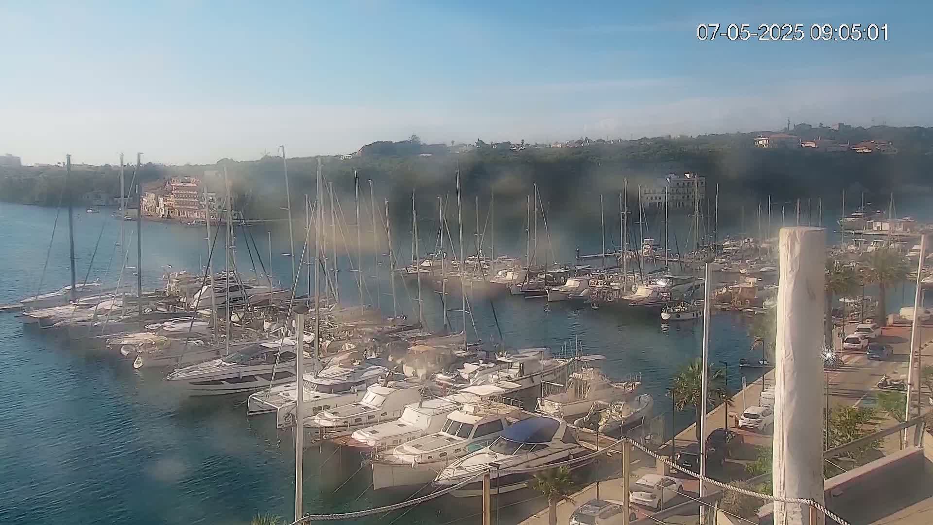 A marina filled with numerous sailboats and motorboats is seen on a hazy, sunny day.