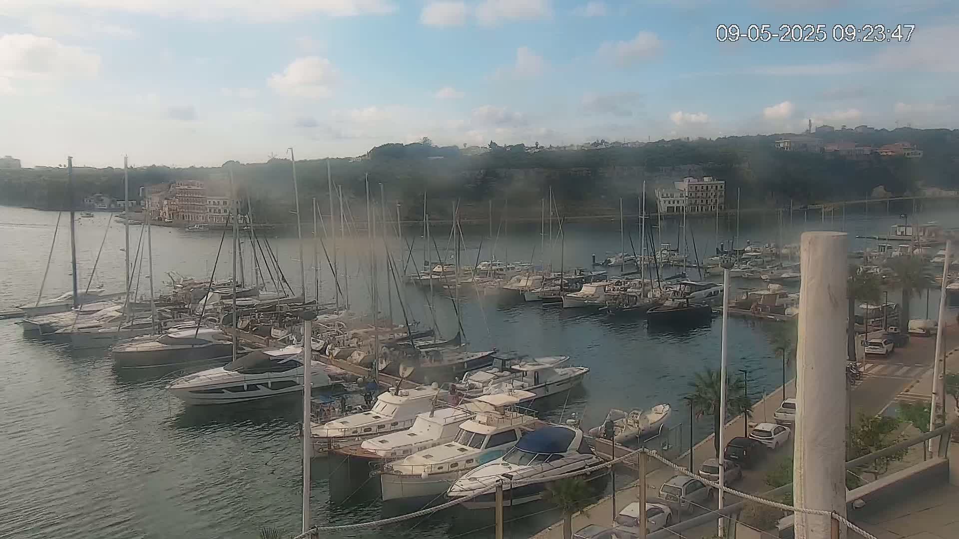 A marina filled with numerous sailboats and motorboats is shown on a partly cloudy day.