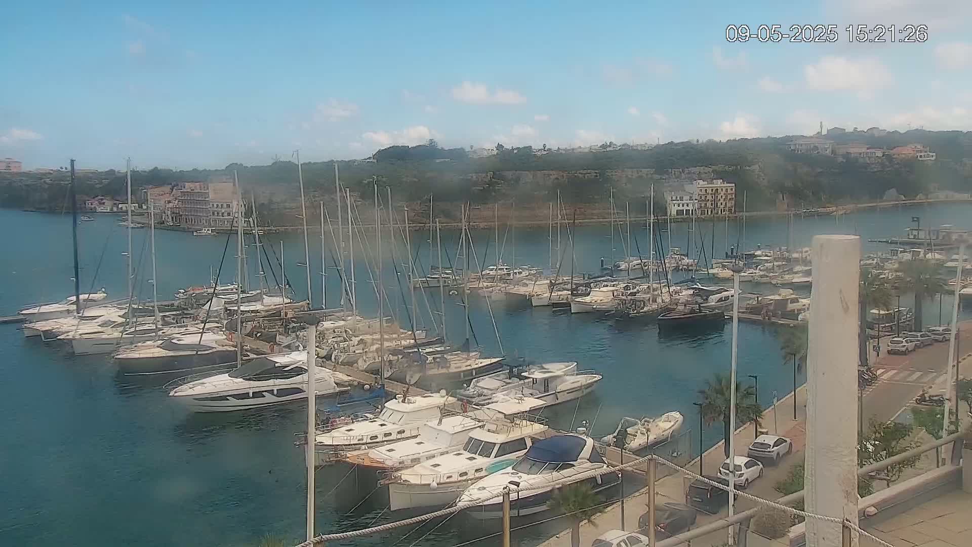 A marina filled with sailboats and motorboats is viewed from above on a partly cloudy day.