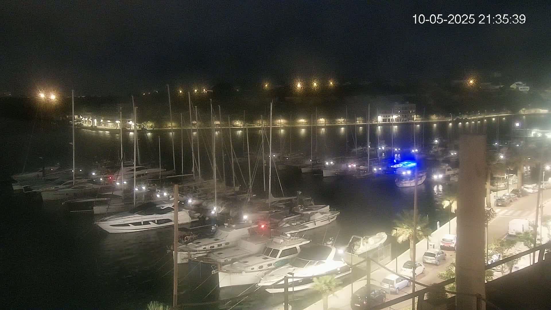 Many boats are docked at a marina at night, illuminated by lights along the shore.
