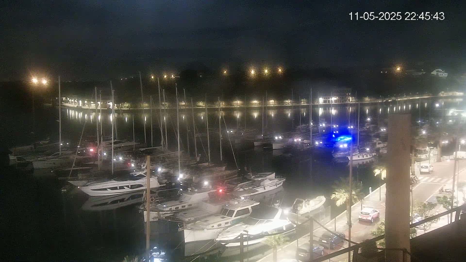 A nighttime view of a marina filled with boats, illuminated by lights along the shore and on the boats themselves.