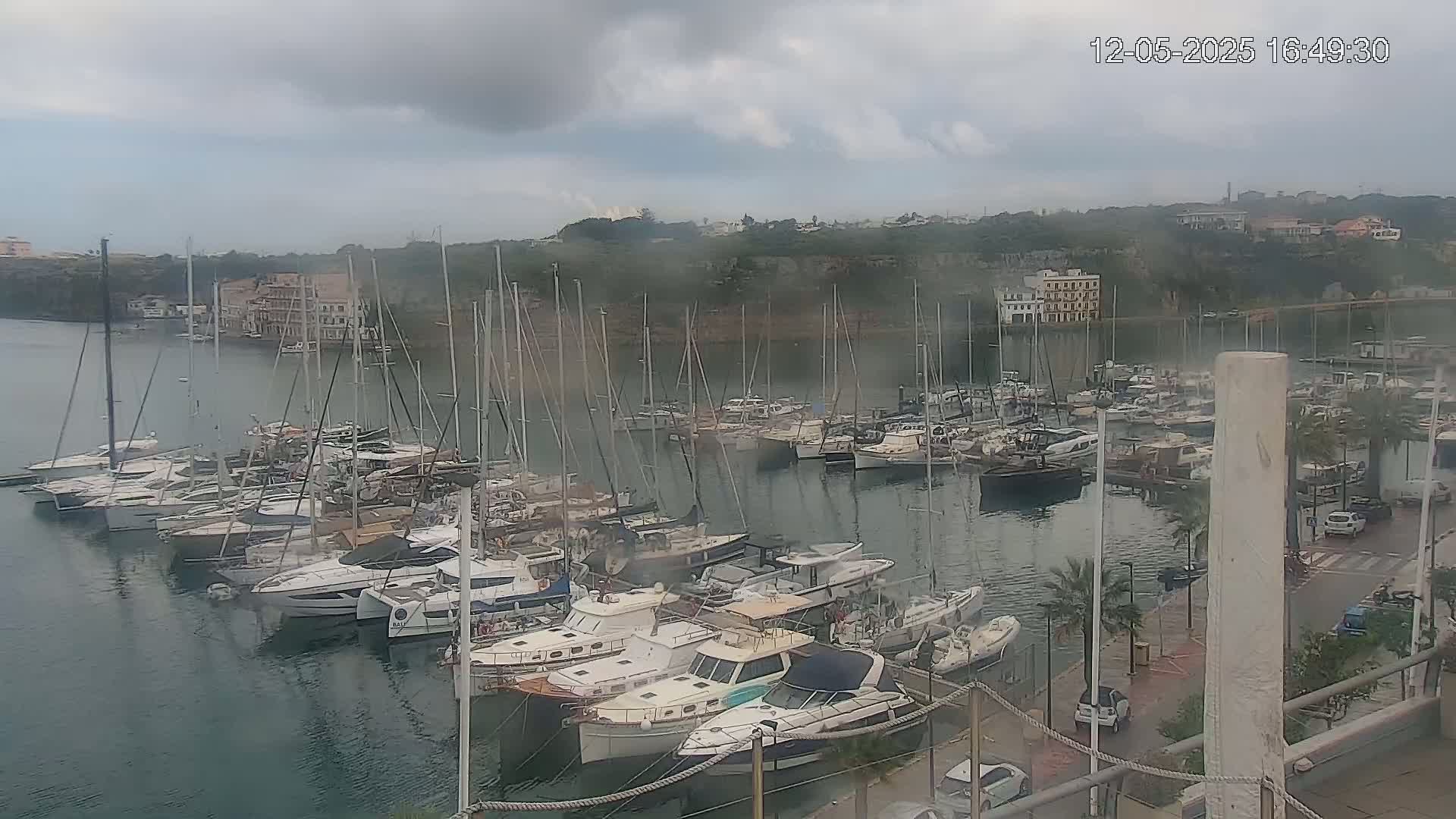 A marina filled with numerous sailboats and motorboats is seen under a cloudy sky.