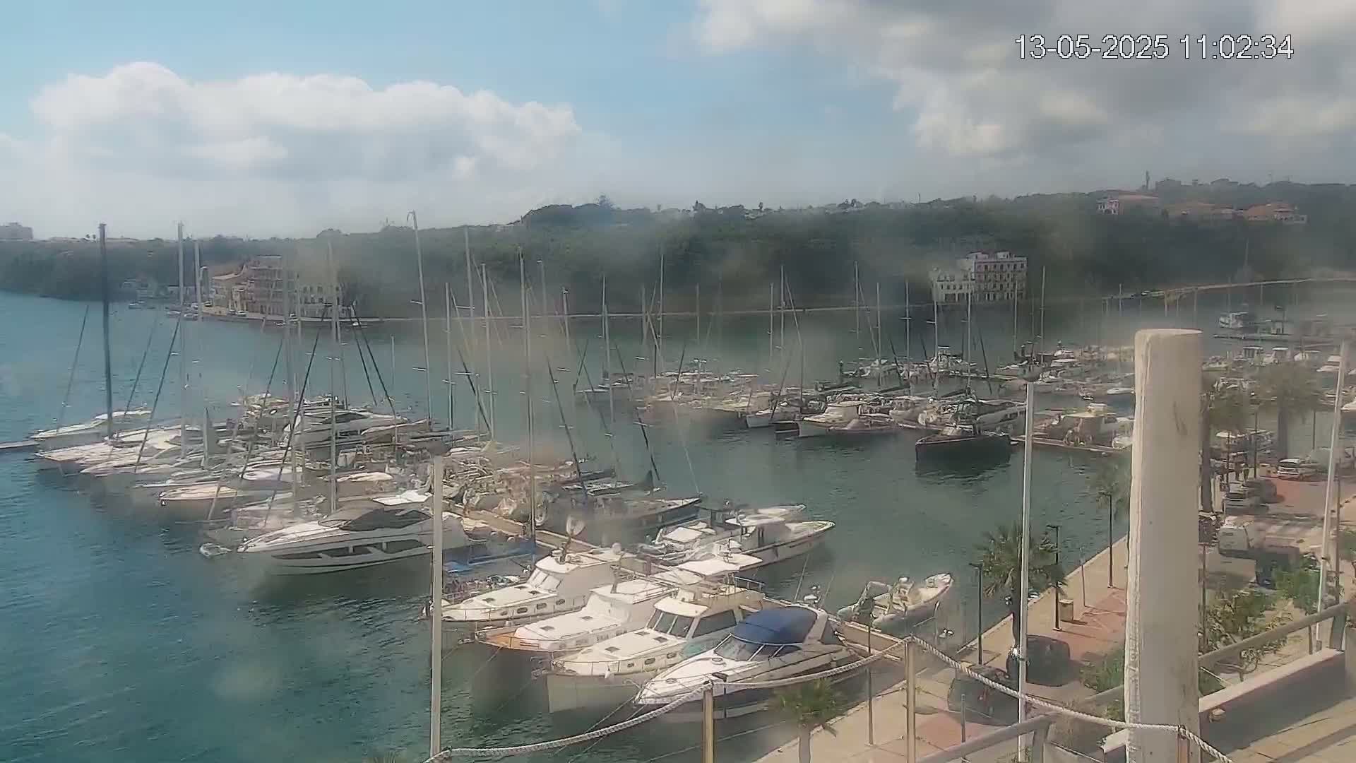 A marina filled with numerous boats and yachts is seen on a partly cloudy day.