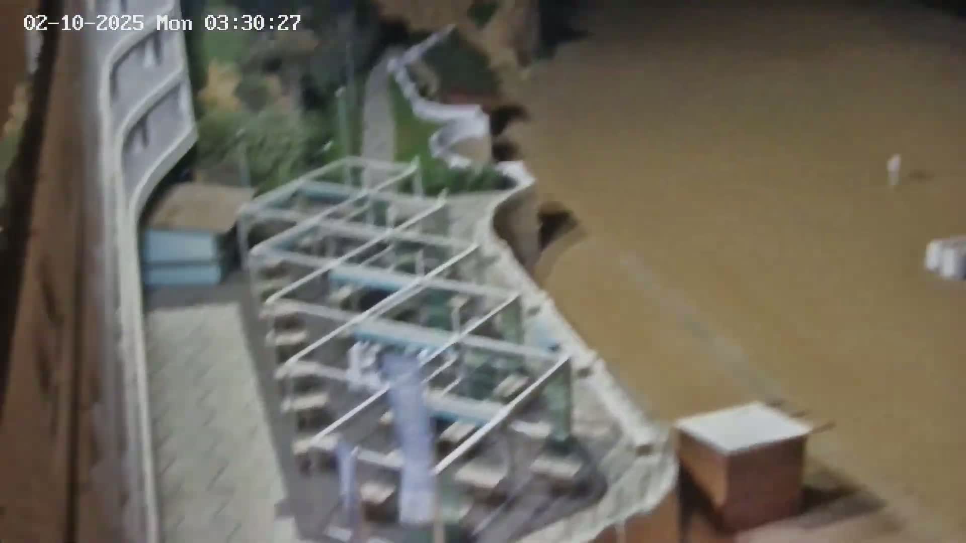 A high-angle nighttime view shows a building partially submerged in muddy floodwaters, with outdoor furniture and structures also underwater.
