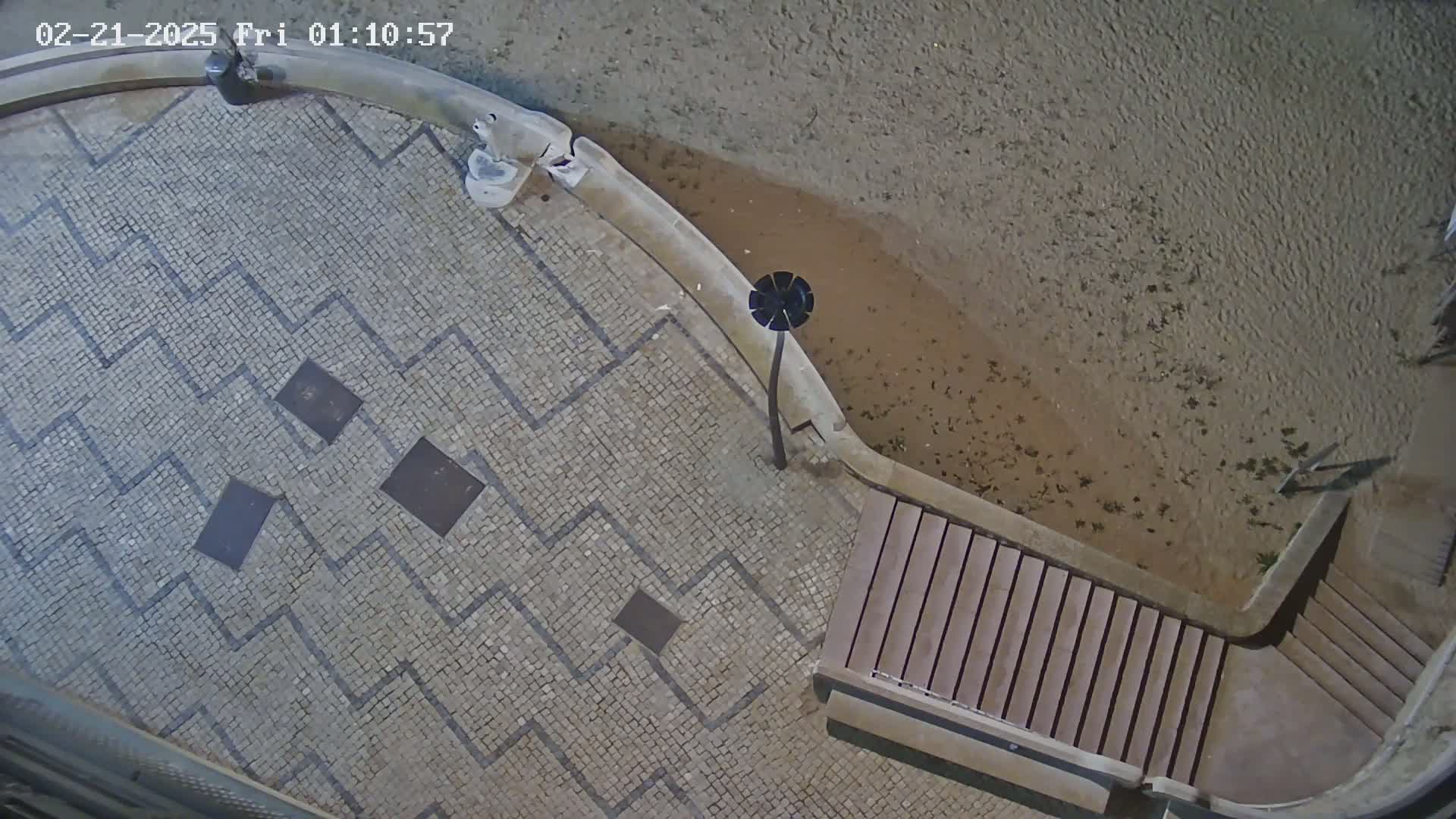 An overhead nighttime view shows a stone plaza with a zig-zag pattern, a lamppost, and wooden steps leading down to a sandy area.