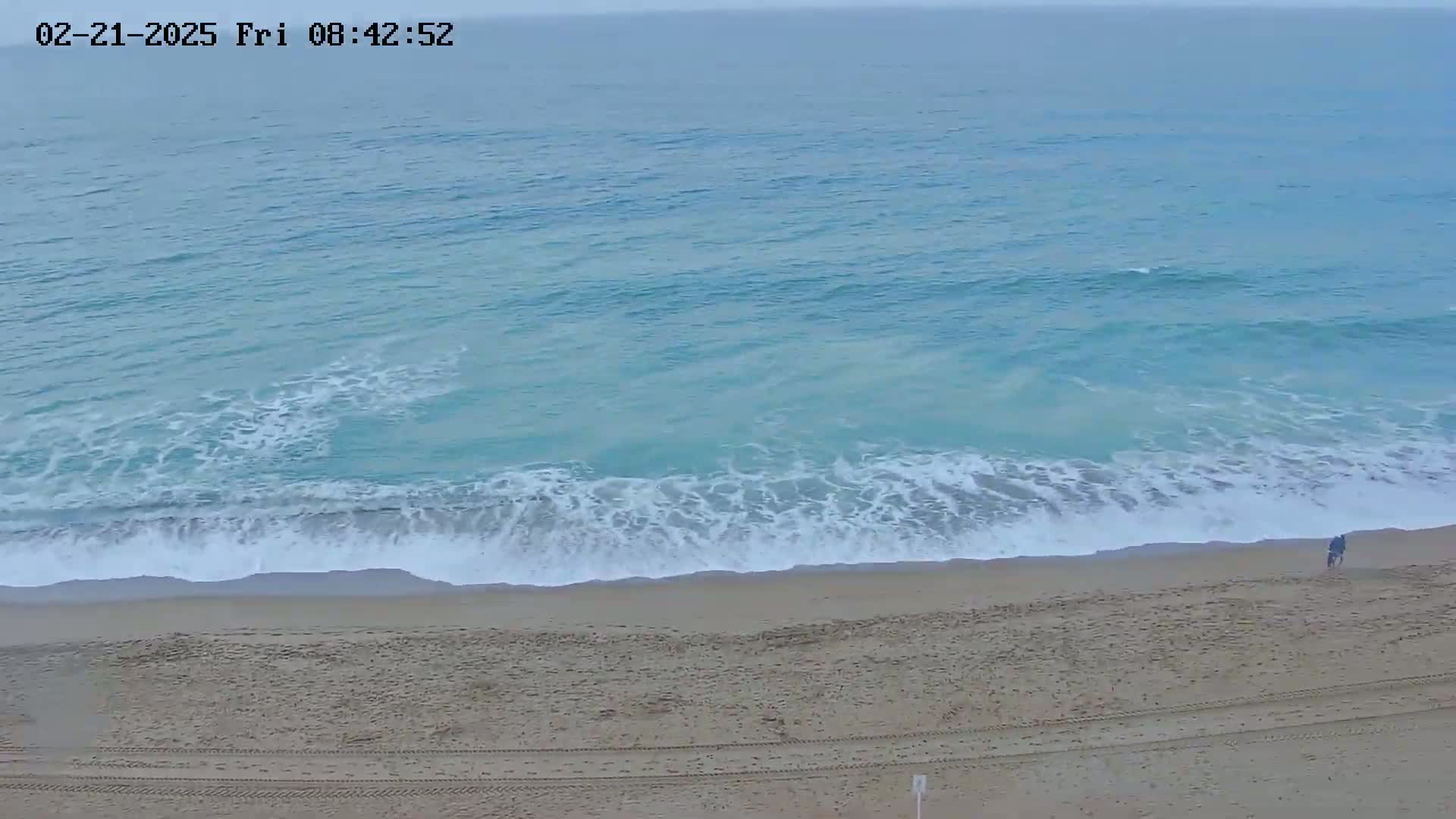 A sandy beach with gentle waves rolling in under an overcast sky.