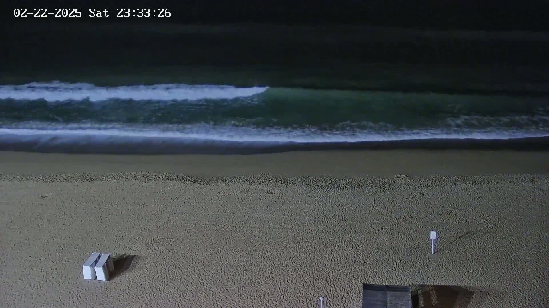 A dark sandy beach at night with gentle waves rolling onto the shore.