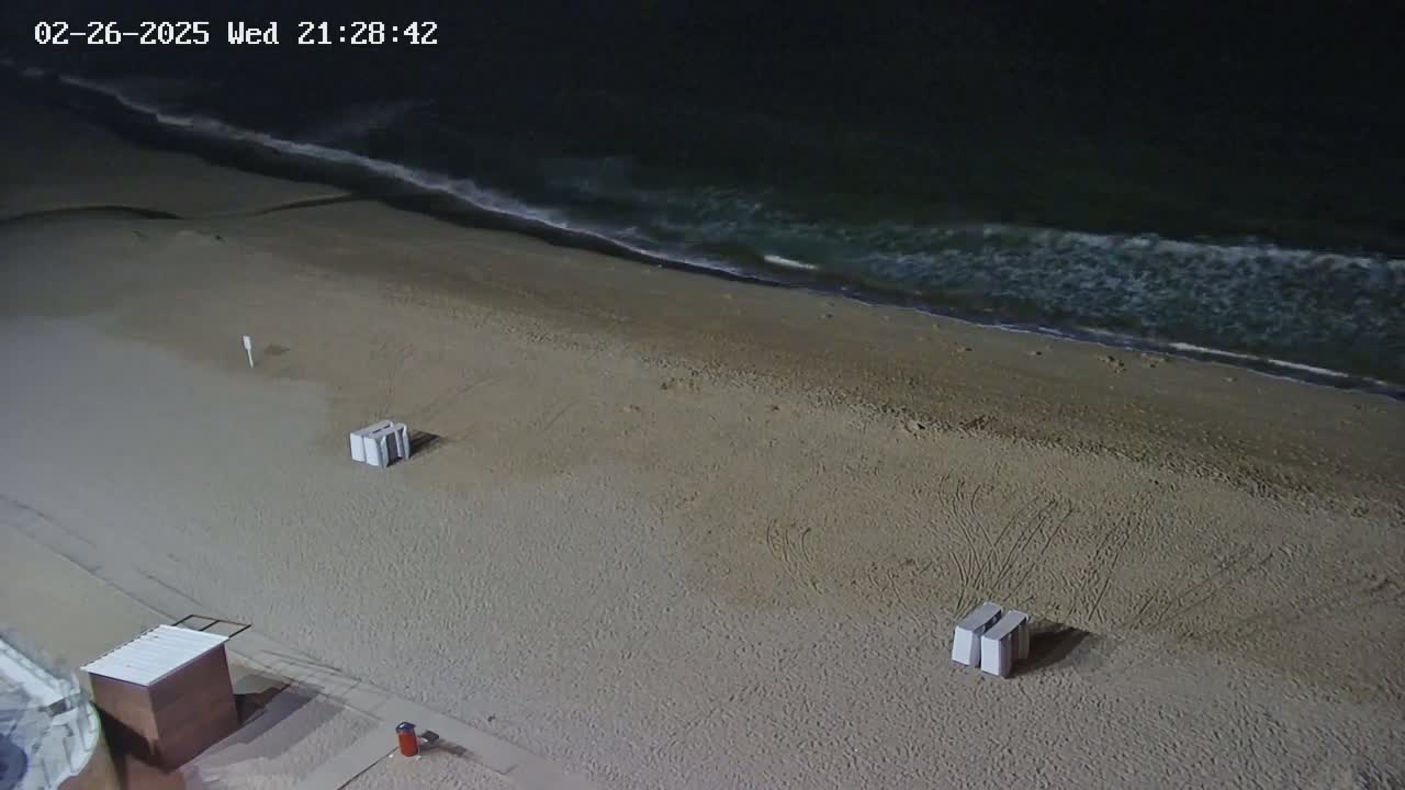 An empty, sandy beach at night is gently lapped by dark ocean waves.
