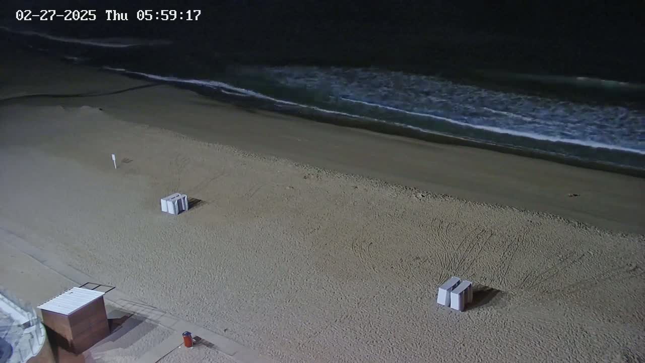 A nighttime view of a mostly empty sandy beach with gentle waves and a few beach structures.