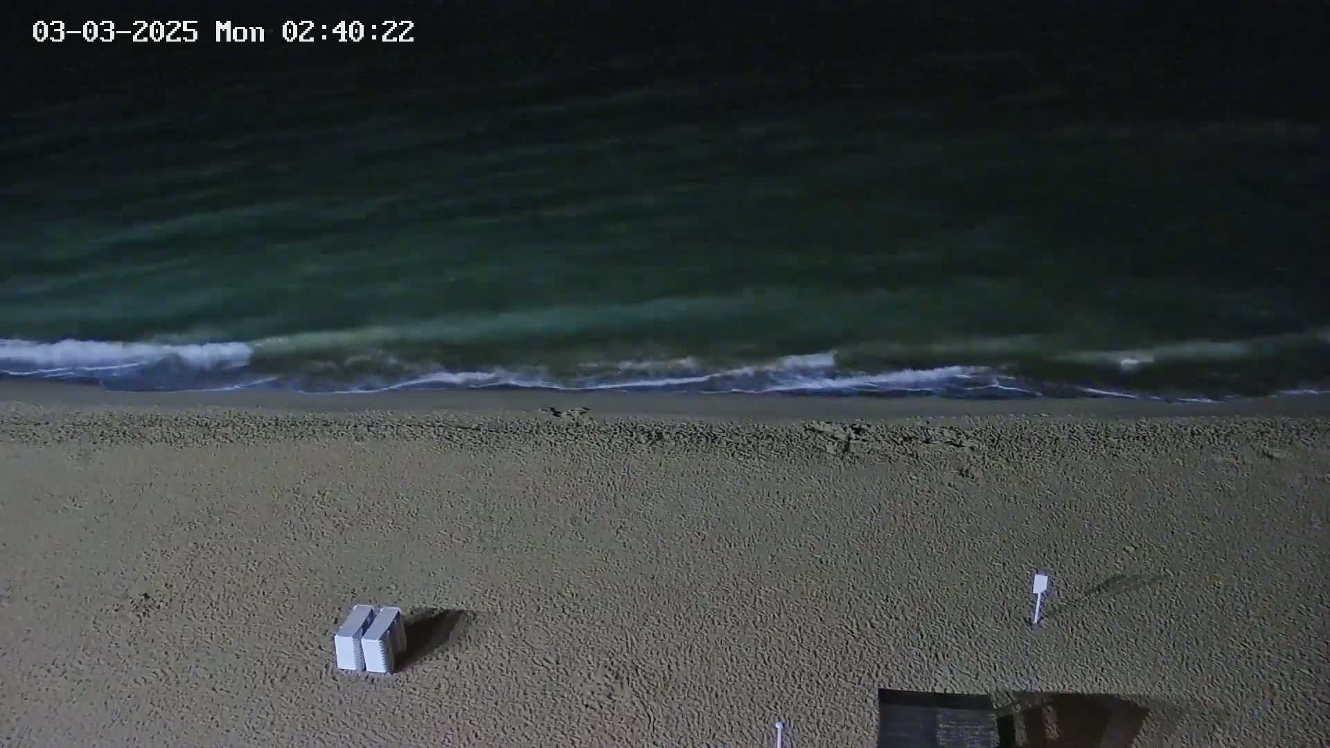 An empty sandy beach at night is gently lapped by dark green waves under a dark sky.