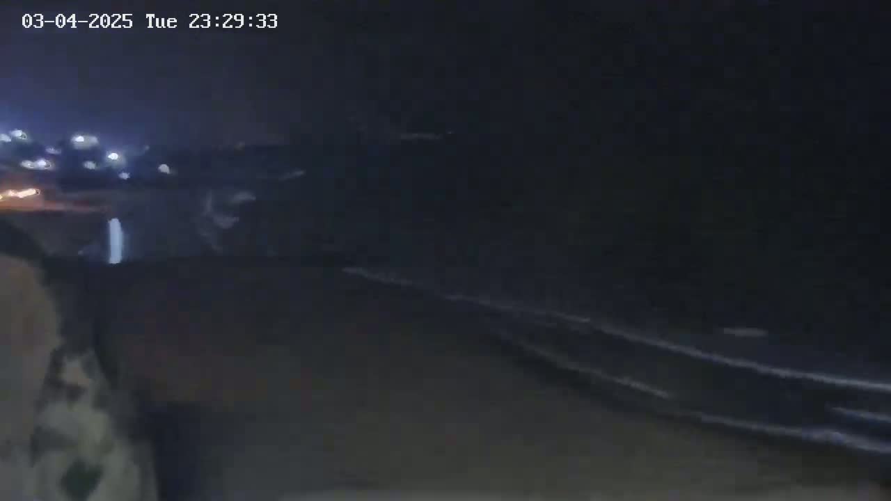 A nighttime, low-light view shows a dark road or path with faintly visible lights in the distance.