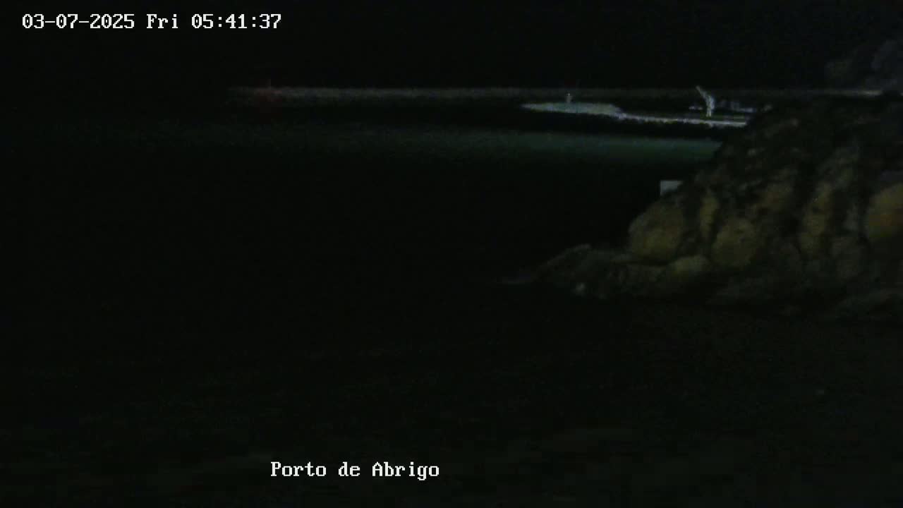 A dark, nighttime scene shows a body of water and a rocky shoreline under a clear, dark sky.