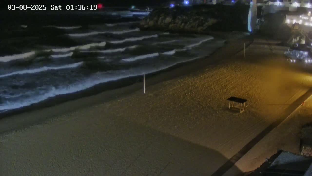 A sandy beach at night with moderate waves rolling onto the shore under dark skies.