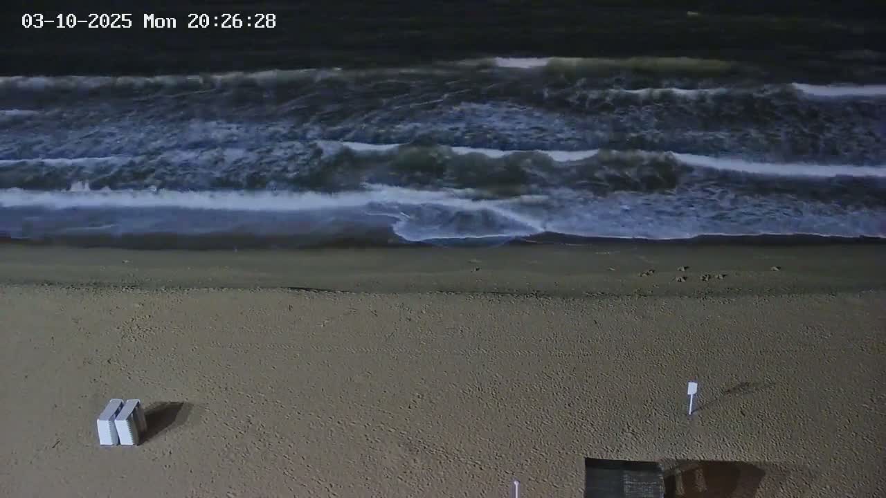 A sandy beach at night with moderately sized waves rolling onto the shore.