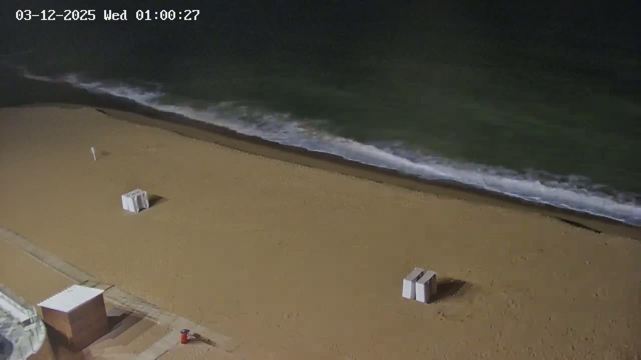 An empty sandy beach at night is gently lapped by dark waves under a dark sky.