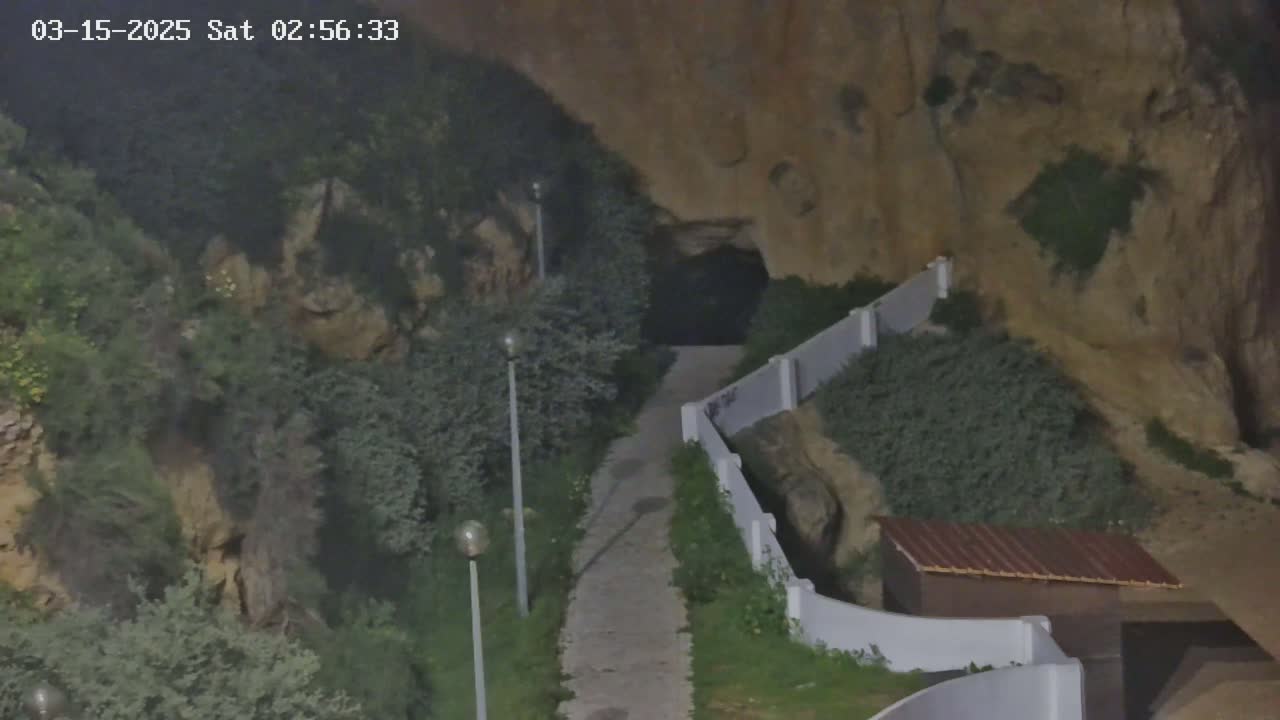 A paved pathway leads to a cave entrance nestled within a rocky hillside under nighttime conditions.