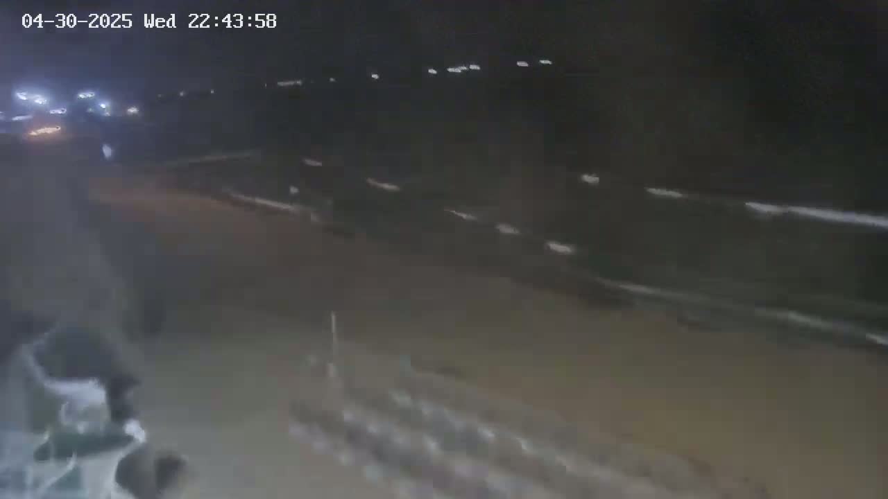 A nighttime, low-light view of a paved area with indistinct vehicles and a blurry object in the foreground.