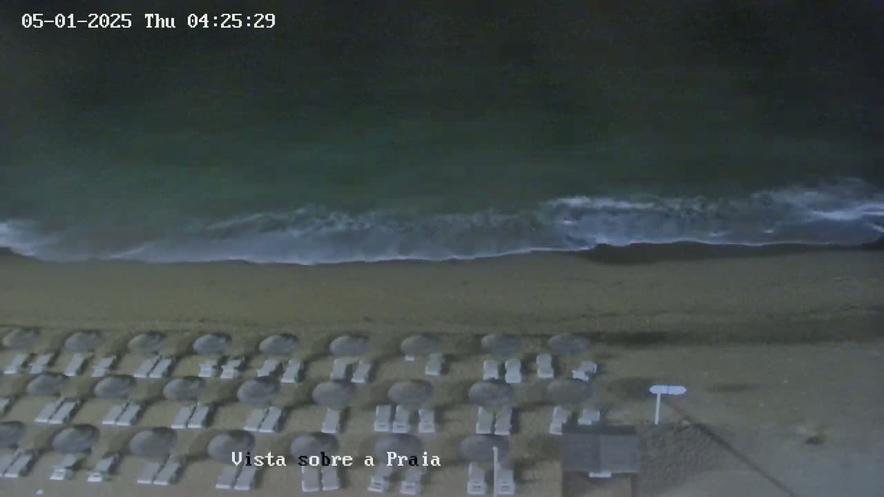 A dark sandy beach at night with gentle waves and rows of closed beach umbrellas.