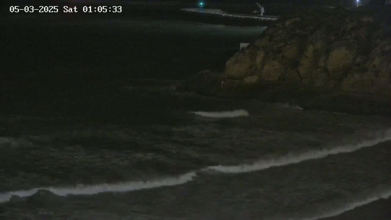 Dark, nighttime waves crash against a rocky shoreline.