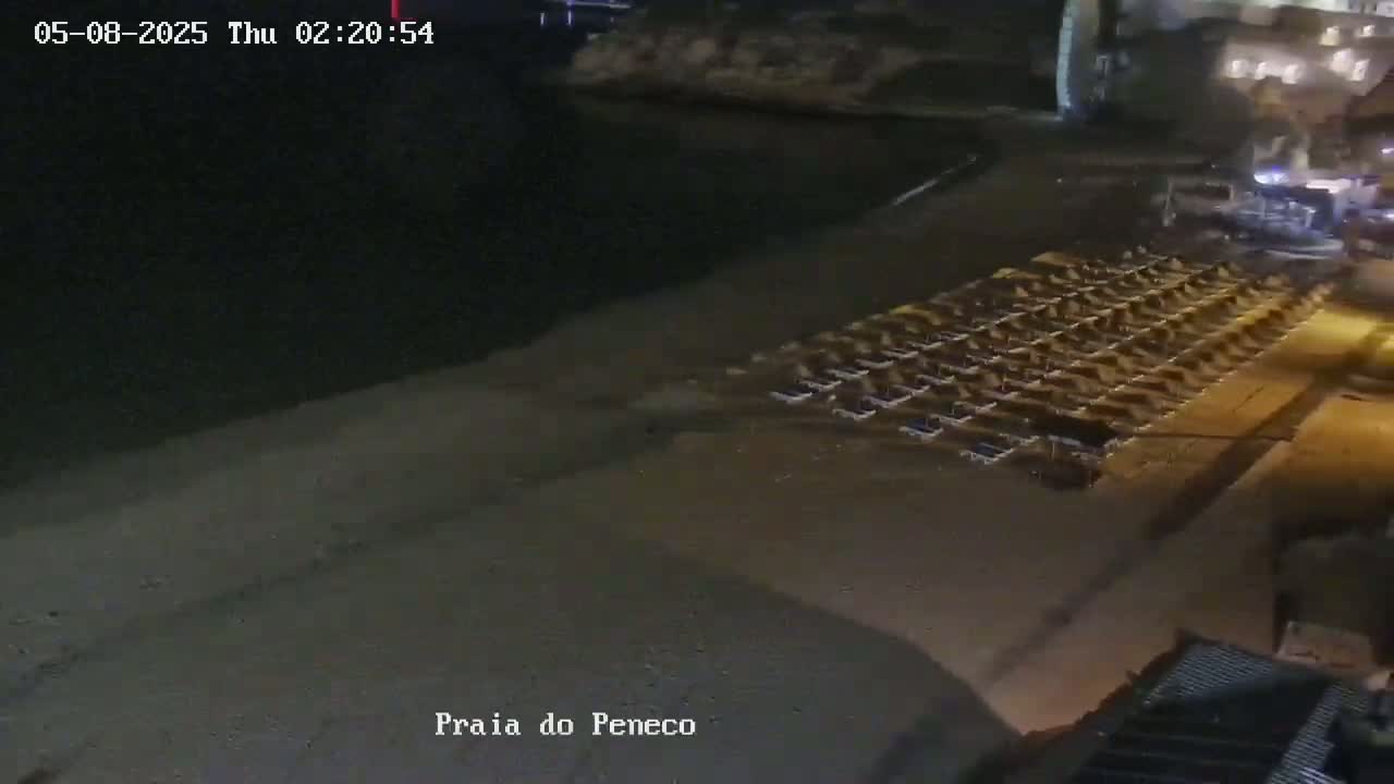 A nighttime, high-angle view shows a beach with many dark objects arranged in rows near the water's edge.