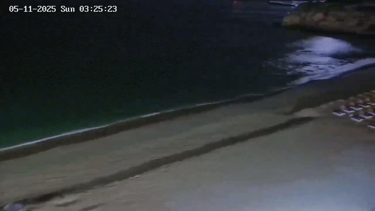 A dark, sandy beach at night is gently lapped by dark water with small waves.