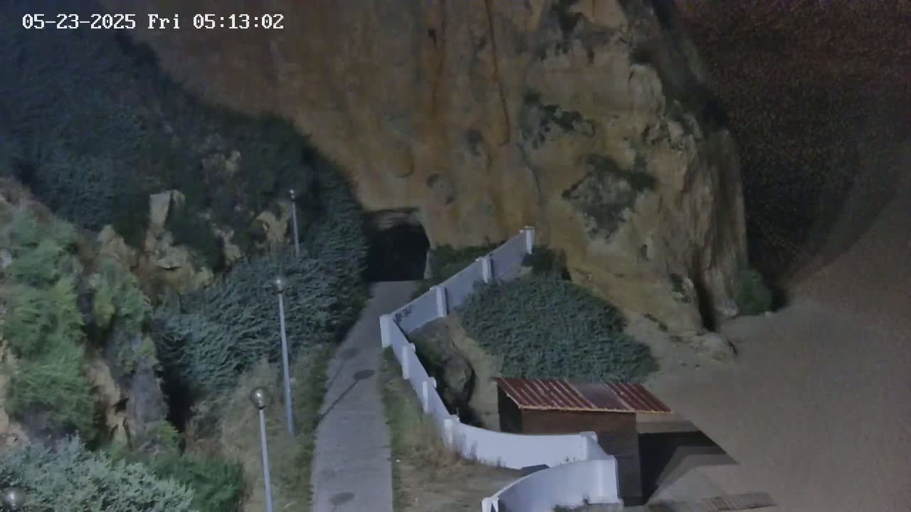 A paved pathway leads to a dark tunnel beneath a rocky cliff at night.