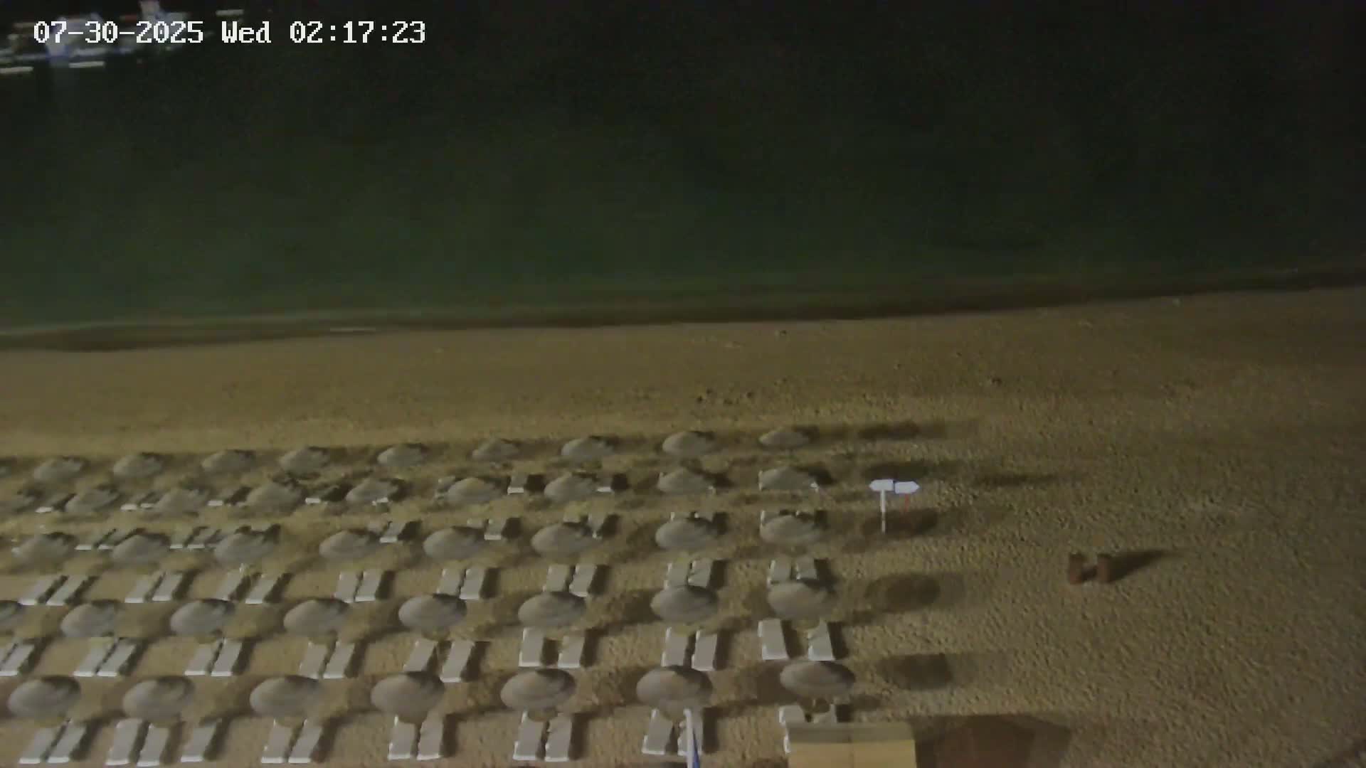 An overhead view shows a sandy area next to a paved walkway with a geometric pattern, a person walking, and a small fountain.