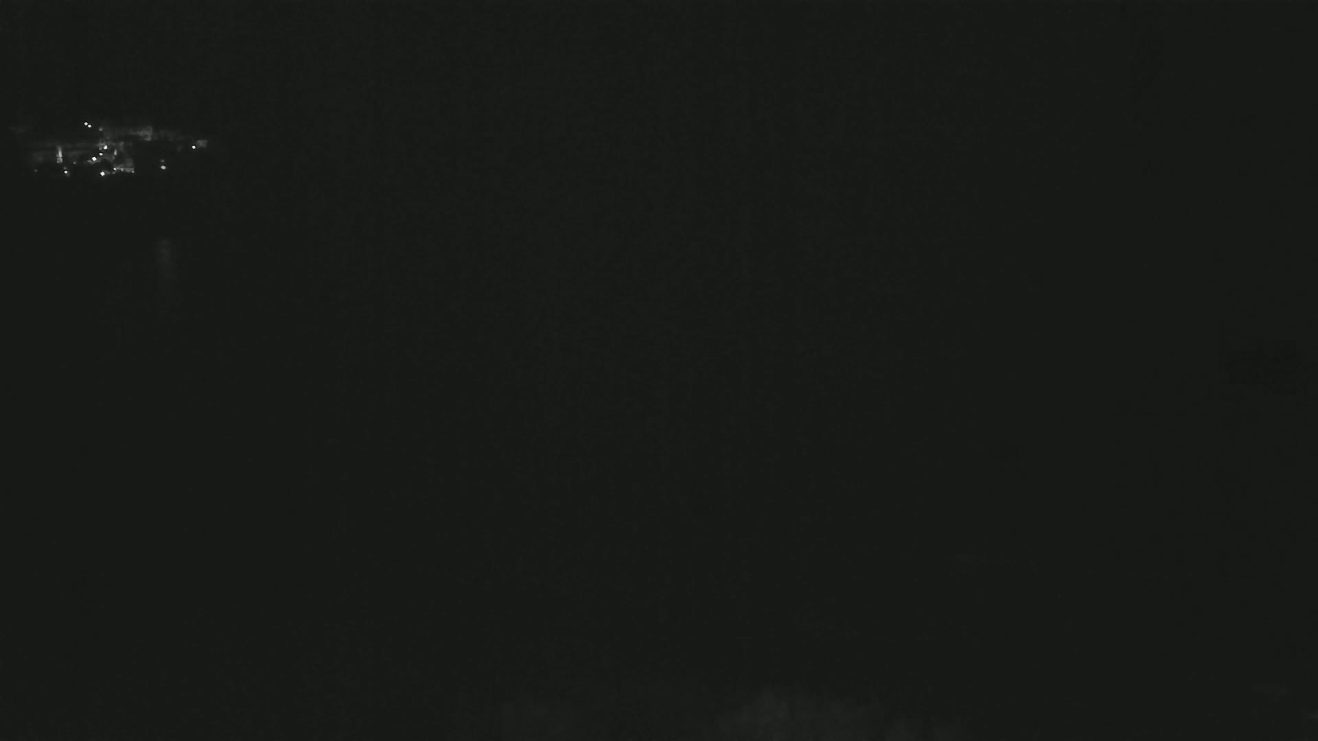 A dark, nighttime scene shows a few faint lights in the distance.