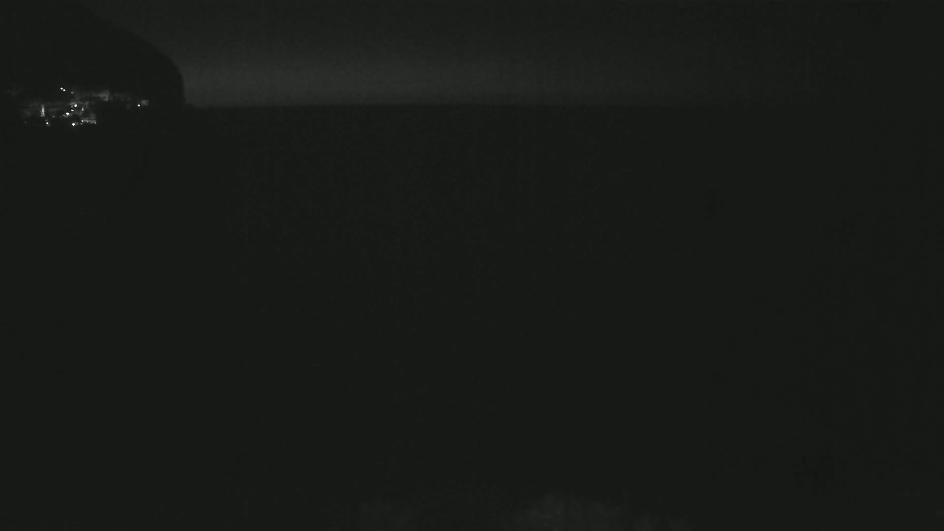A dark, nighttime scene shows a dimly lit coastline with a body of water extending to a dark horizon.