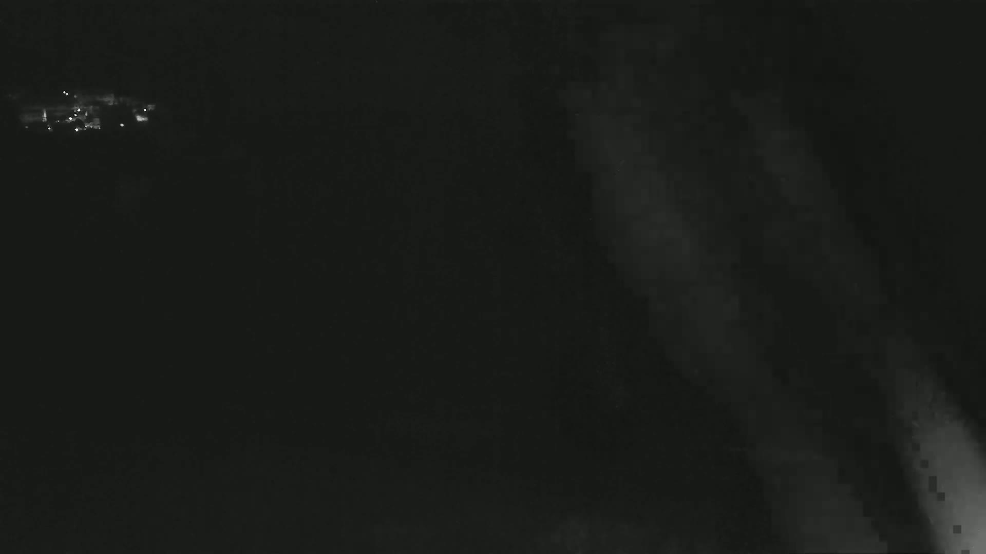 A dark, nighttime scene shows faintly lit buildings in the distance and a hazy, possibly smoky or foggy atmosphere in the foreground.