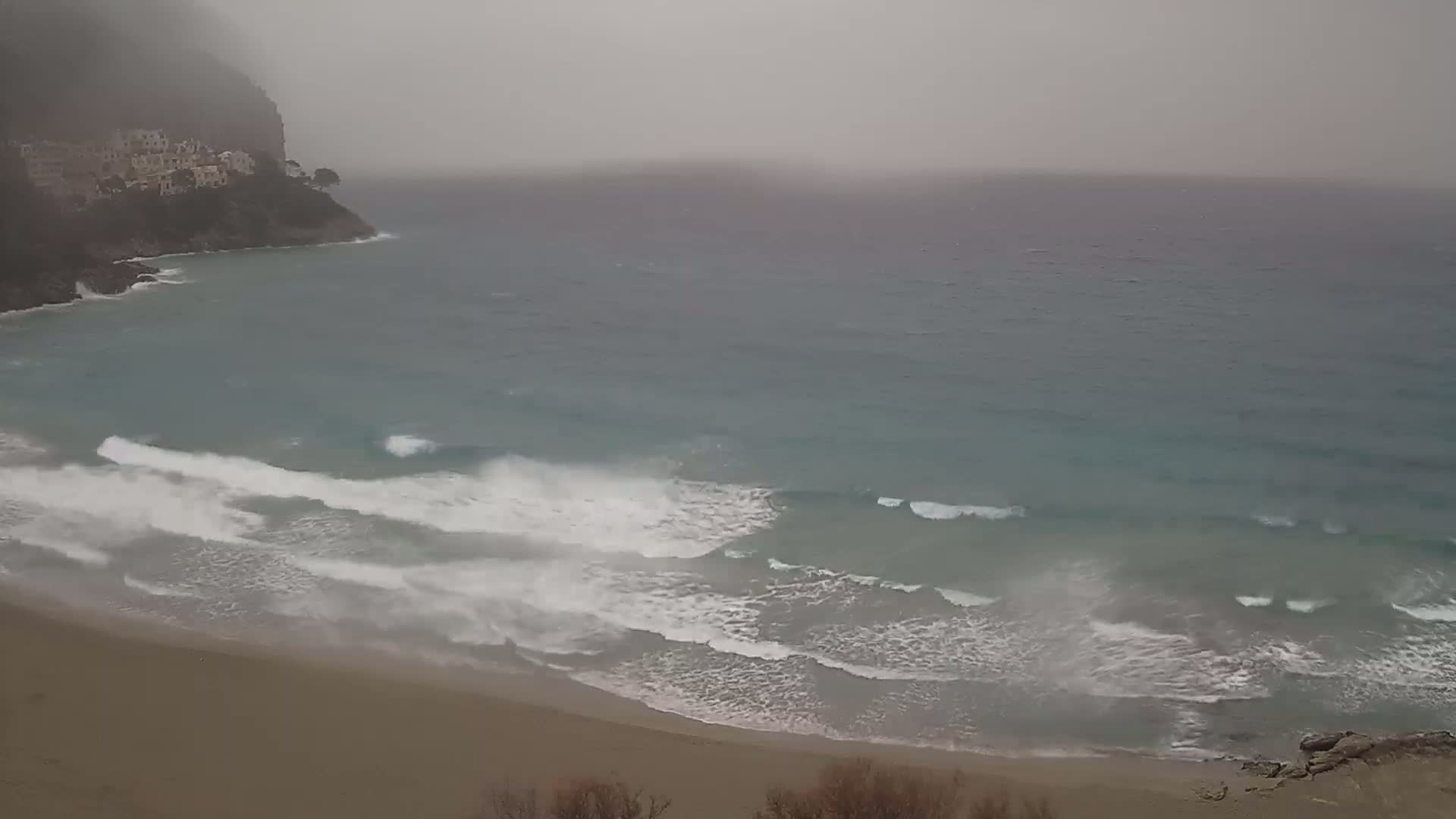 A sandy beach with moderate waves crashes on the shore under an overcast sky.