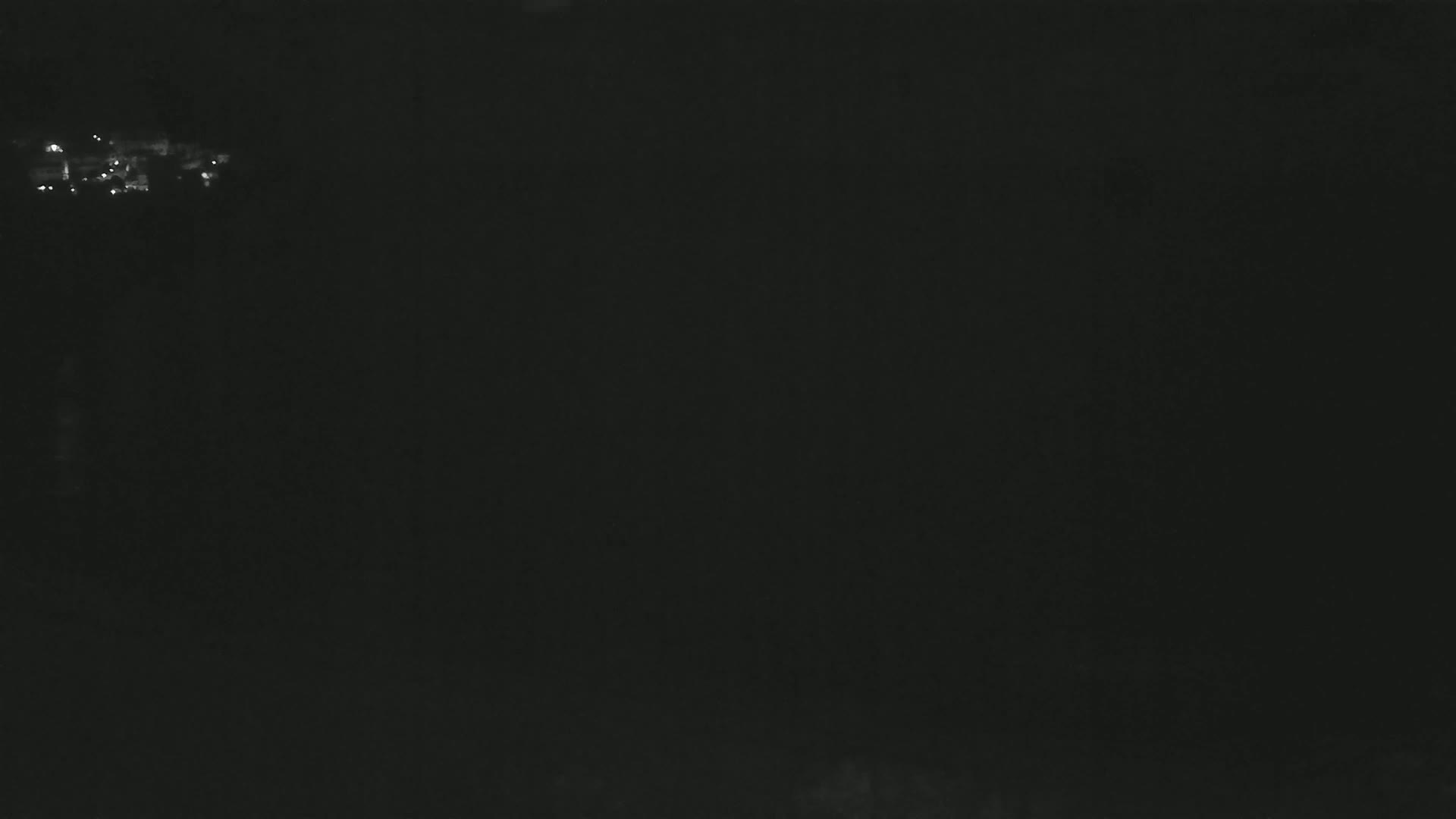 A dark, nighttime scene shows a few faint lights in the distance.