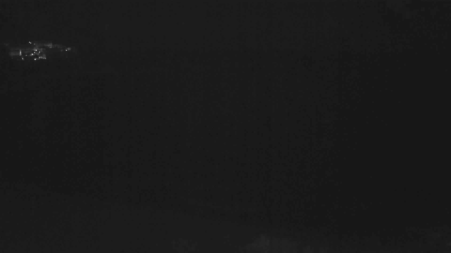 A dark, nighttime scene shows a few faint lights in the distance.