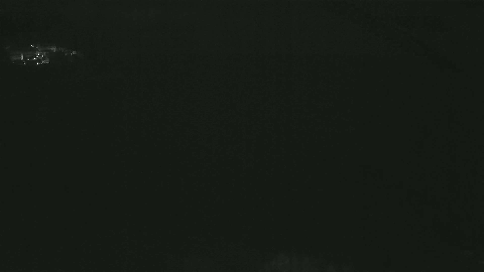A dark, nighttime scene shows a small cluster of faint lights in the distance.