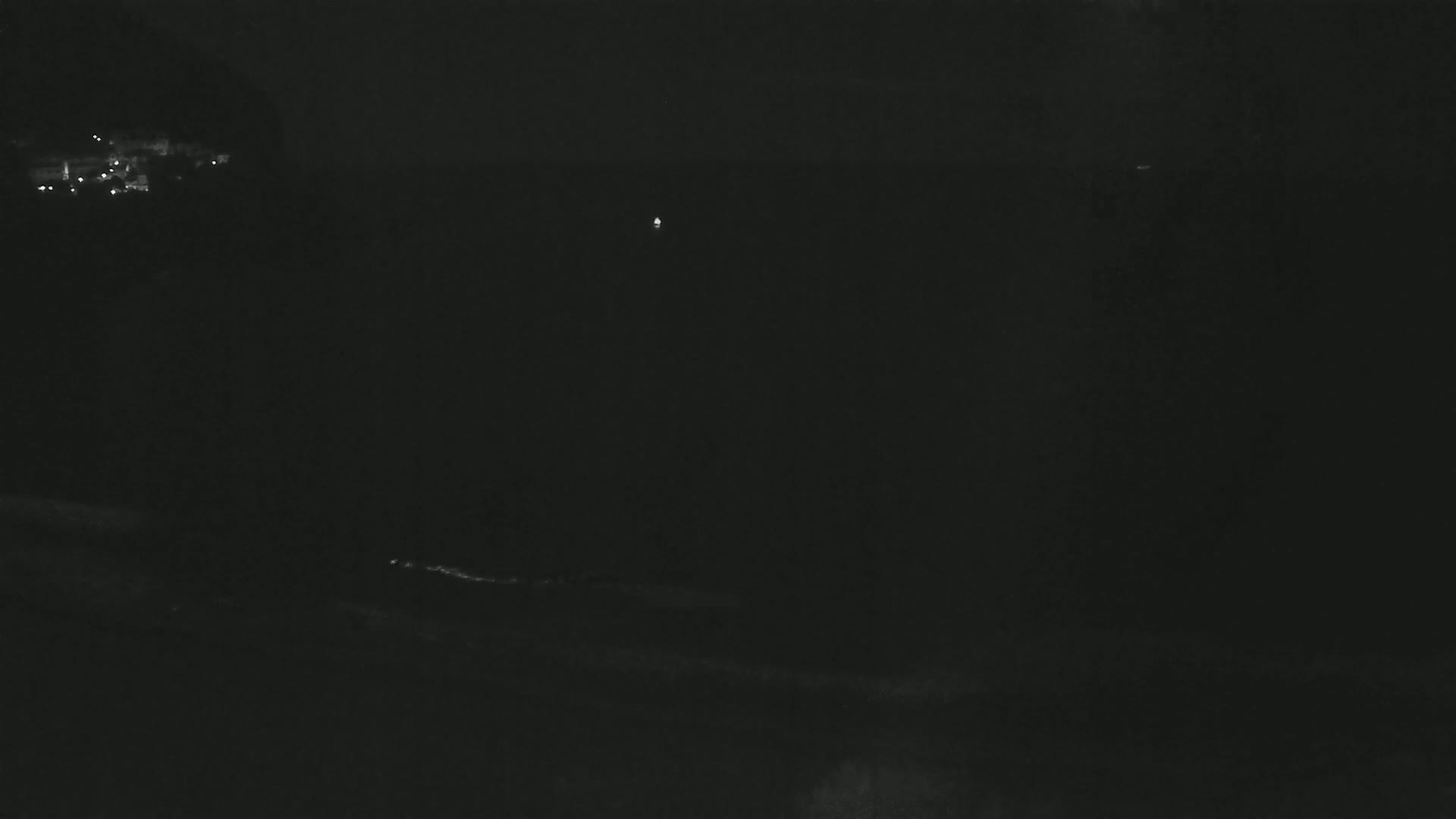 A dark, nighttime scene shows a distant collection of faint lights, possibly a town, and a single, brighter light in the middle distance.