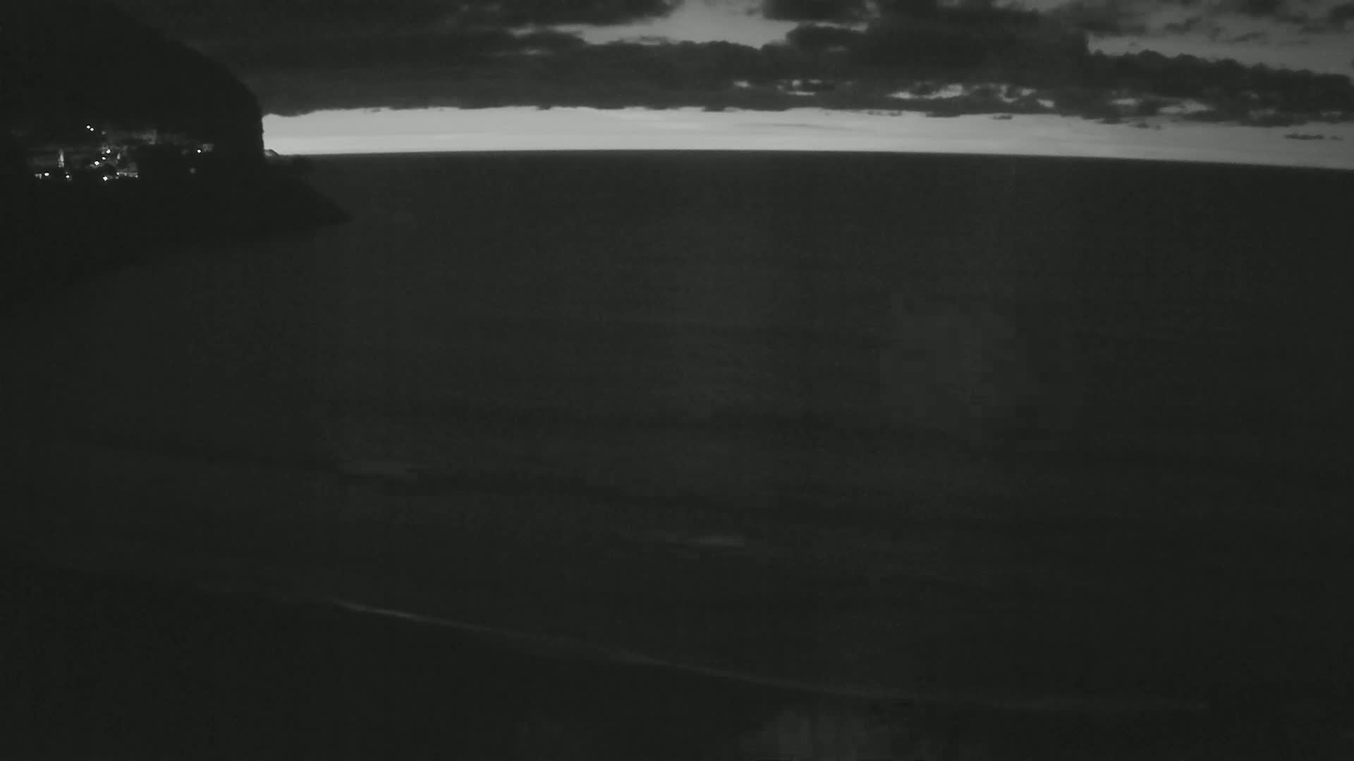 A dark, cloudy night scene shows a body of water extending to a faintly lit horizon, with a dimly lit landmass visible on the left.