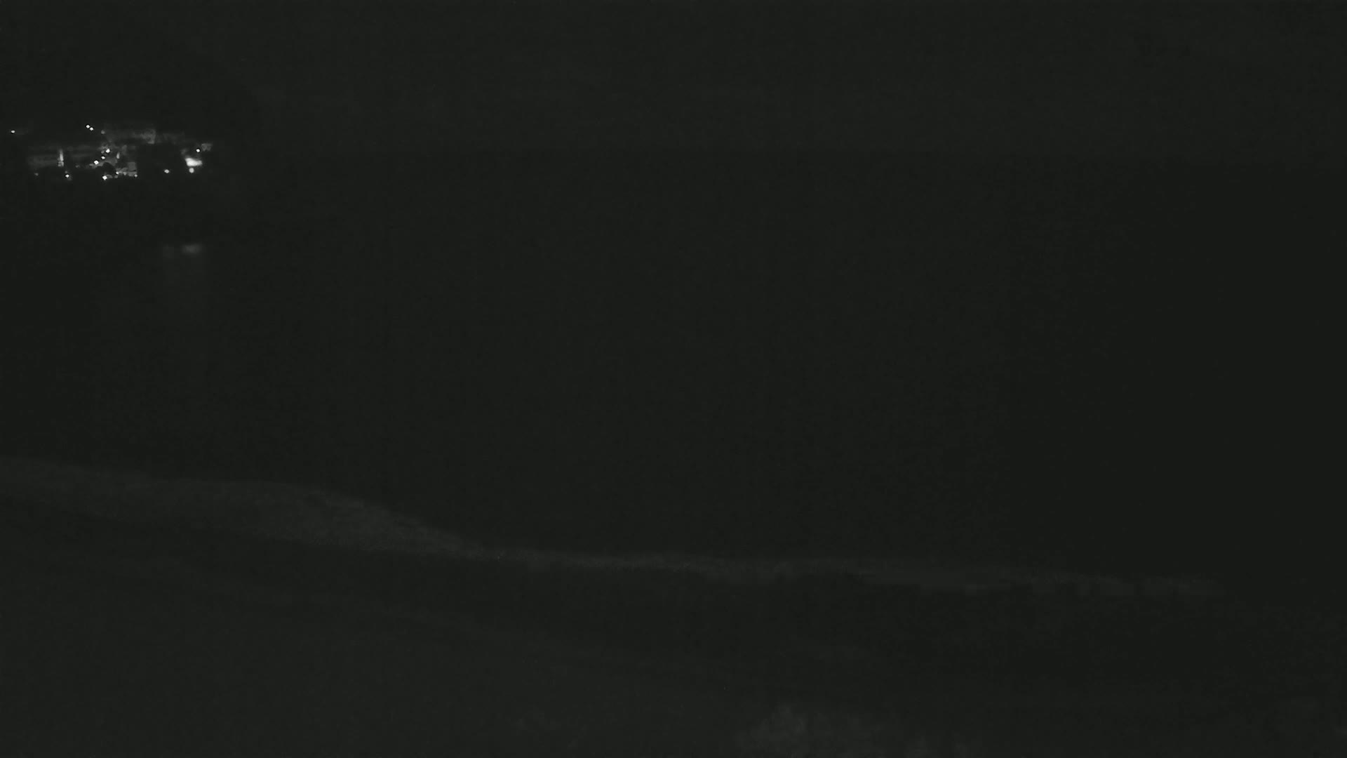 A dark, nighttime landscape shows a distant cluster of lights and a dark body of water in the background.
