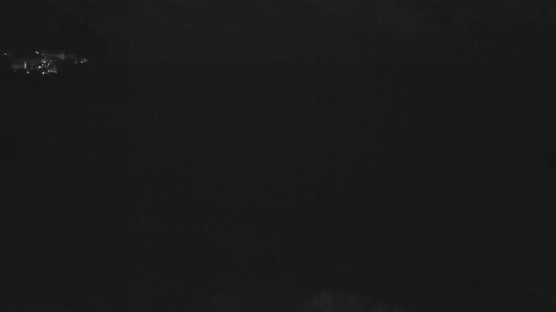 A dark, nighttime scene shows a small cluster of faint lights in the distance.