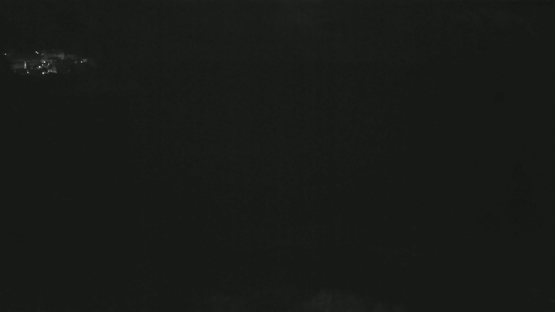 A dark, nighttime scene shows a few faint lights in the distance.